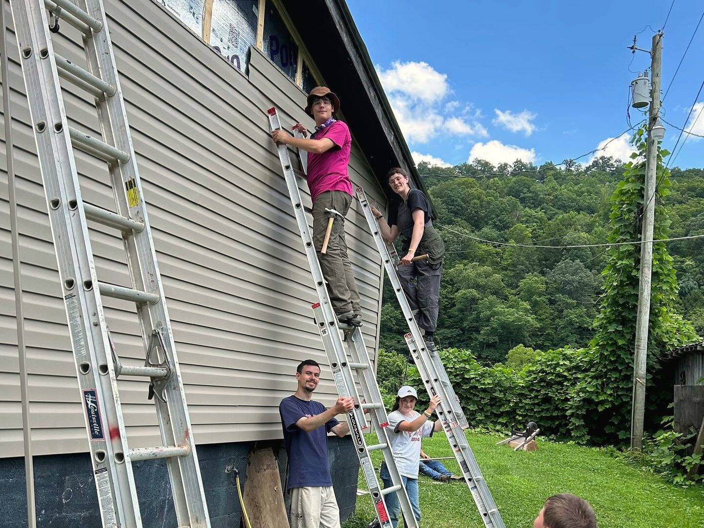 Volunteers on ladders replacing siding on a neighbor's home